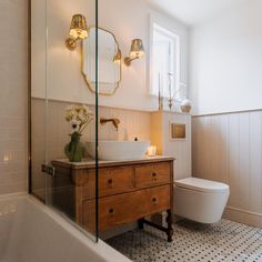 a white toilet sitting next to a bath tub under a bathroom mirror above a sink