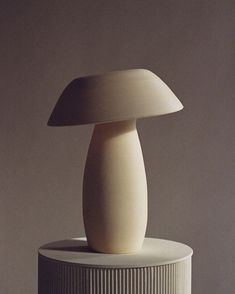 a white vase sitting on top of a table next to a light brown wall behind it