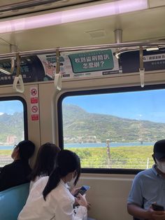 two people sitting on a train looking at their cell phones while the other person is wearing a face mask