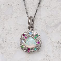 Our pebble collection of raw, rough, beaten metals set with precious gems. Perfectly imperfect and all one of a kind. A crystal opal is surrounded by pink sapphires, emeralds and aquamarines and is set into a pebble disc necklace. Pebble measures 13.5mm round approx. Pendant weighs 4.8g approx. If ordering with a chain, the chain measures 45cm. Please note if ordering the white gold it is raw with a matte finish and not rhodium plated. Gemstone Jewelry With Ethiopian Opal Round Pendant, Ethiopian Opal Gemstone Pendant Jewelry, Opal Multi-stone Pendant Necklace, Pebble Collection, Painters Palette, Crystal Opal, Aqua Marine, Disc Necklace, Precious Gems