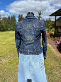 a woman's jean jacket on display in front of a grassy area with flowers