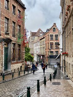 people are walking down the cobblestone street in an old european city with tall buildings