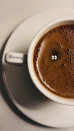 a cup of coffee on a saucer with the word morning written in it and a spoon