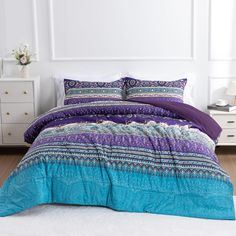 a bed with purple and blue comforters in a room next to a white dresser