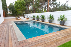 an empty pool surrounded by wooden decking and potted plants on the side of it