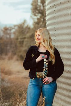 a beautiful blonde woman standing next to a tall metal structure wearing jeans and a black jacket