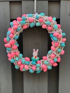 a wreath decorated with pink, blue and white eggs is hanging on a wooden fence