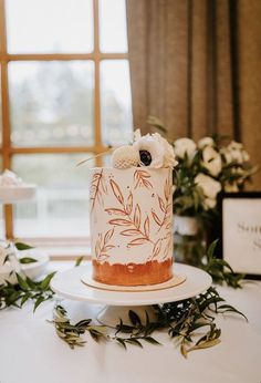 a wedding cake sitting on top of a table next to white flowers and greenery