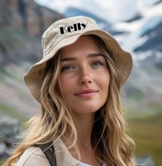 a woman wearing a hat with the word kelly on it in front of some mountains