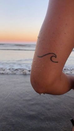 a woman's foot with a wave tattoo on it, in front of the ocean