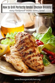 grilled chicken breast on a plate with salad and lemon wedges