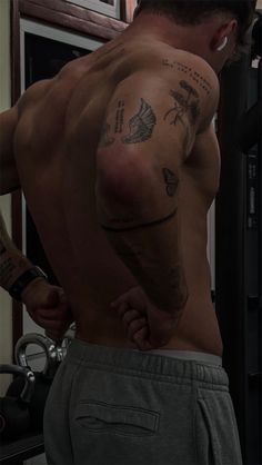 a shirtless man with tattoos on his arm and chest standing in front of a mirror