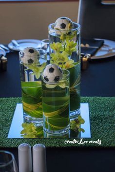 two vases filled with flowers and soccer balls on top of a grass covered table