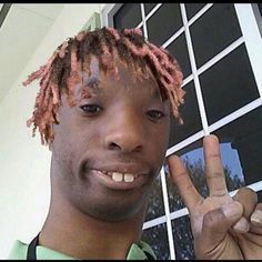 a young man with dreadlocks making the peace sign in front of a window