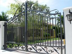 an iron gate is shown in front of a white wall and fenced driveway area