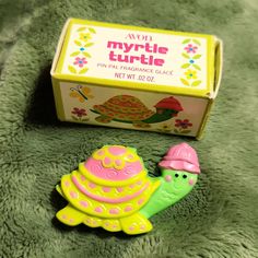 a small toy turtle sitting next to a box on a green surface with flowers and leaves