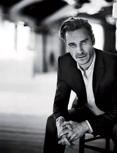 a black and white photo of a man in a suit sitting on a wooden bench