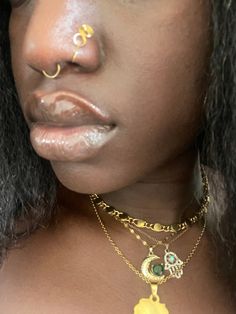 a close up of a person wearing a gold necklace and nose ring with an evil look on their face