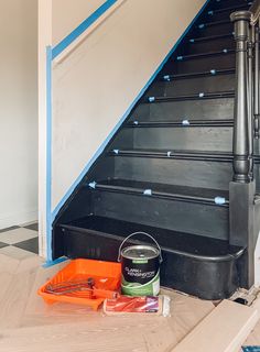 a can of paint sitting on the ground next to some stairs with blue tape around it