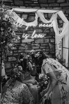 black and white photo of two women sitting in front of a sign that says, all you need is love