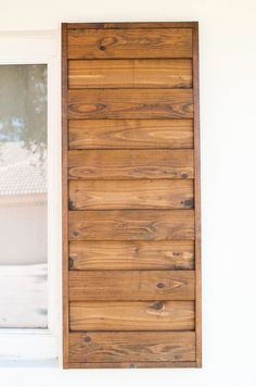 an open window with wooden slats on the outside and side of it, in front of a white wall