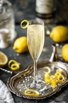 a glass filled with champagne sitting on top of a silver tray next to lemons