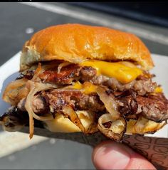 a hand holding a cheeseburger with meat and onions