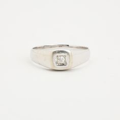 a white gold ring with a square diamond set in the center, on a plain surface