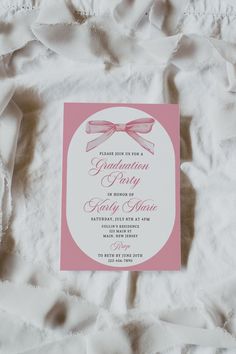 a pink and white wedding card with a bow on it's side sitting on a bed