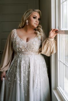 a woman standing next to a window wearing a dress