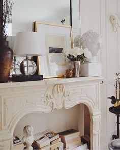 a white fireplace mantel with flowers and pictures on it, along with other decor items