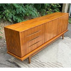 a large wooden cabinet sitting on top of a rug in front of some bushes and trees