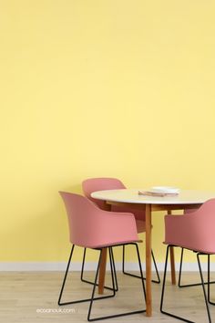 two pink chairs and a white table against a yellow wall