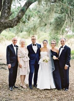 a group of people standing next to each other in front of some trees and bushes