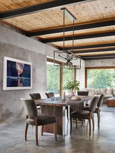 a dining room table surrounded by chairs in front of a large window with wood beams