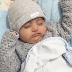 a baby is laying down wearing a gray hat and grey mittens on his head