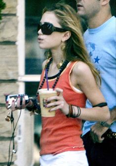 a man and woman are walking down the street with drinks in their hands while wearing sunglasses