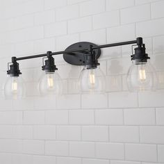 a bathroom light fixture with five bulbs on the wall and white brick walls behind it