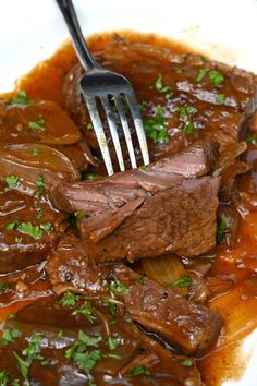 a white plate topped with beef and potatoes covered in gravy next to a fork