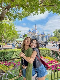 two girls hugging each other in front of the castle at disneyland world with flowers all around