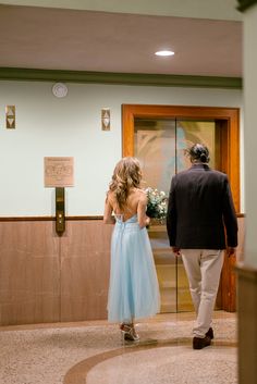 a woman in a blue dress and a man in a suit walking into a building