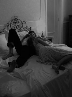 two people laying on a bed in a room with white walls and flooring, one person has her feet up on the edge of the bed