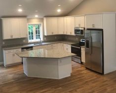 an empty kitchen with stainless steel appliances and white cabinets, wood floors, and hard wood flooring