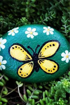 a painted rock sitting in the grass with daisies and a yellow butterfly on it