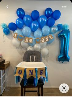 blue and white balloons are hanging from the wall above a baby's high chair