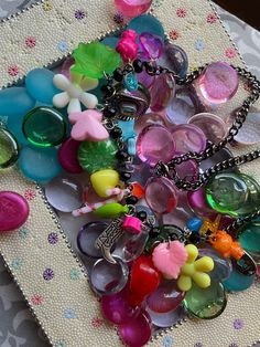 a bunch of different colored buttons on a white table cloth with some silver chains attached to them