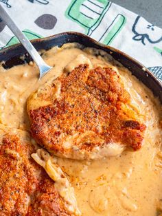 two pieces of meat covered in gravy on top of a skillet with a spoon