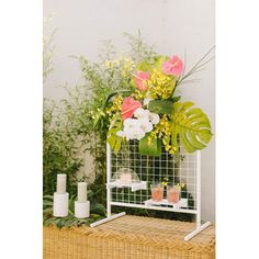 a table with flowers and candles on it in front of a planter filled with greenery