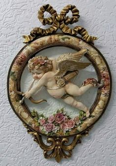 an angel statue is hanging on the wall in front of a circular frame with flowers