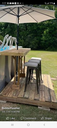 an outdoor table and chairs under an umbrella on a wooden deck in front of a swimming pool